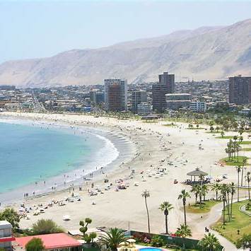 Panorámica de Playa Cavancha en Iquique, Región de Tarapacá, con arena clara, palmeras y aguas templadas del Pacífico, ideal para escapadas costeras en el norte de Chile.